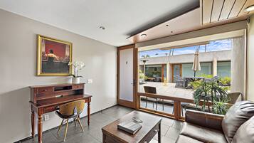 Un salón moderno con un escritorio de madera, un sofá cómodo y un amplio ventanal con vistas al patio exterior.