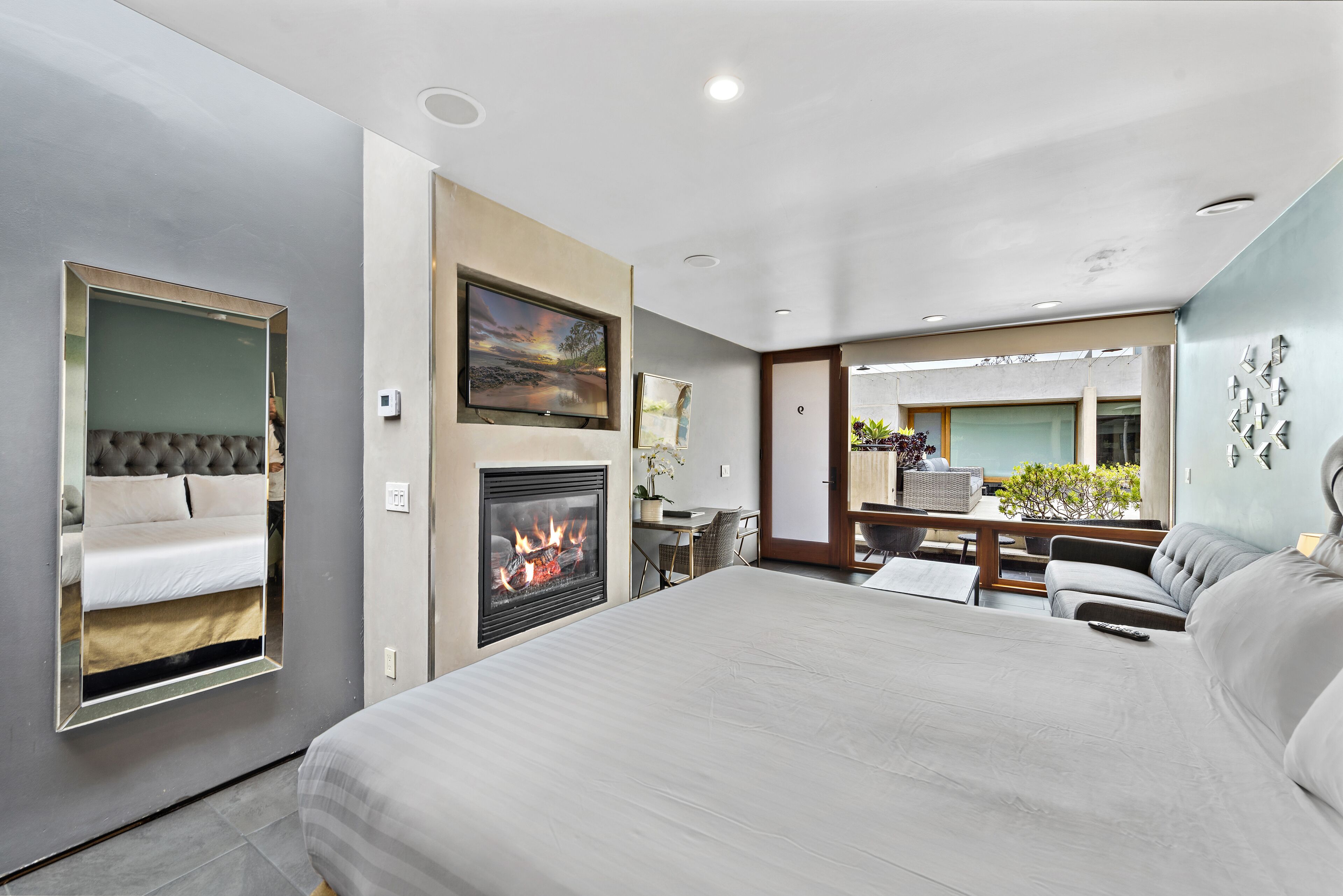 A modern bedroom with a large bed, a fireplace, a desk, and a seating area with a view of the outdoors.