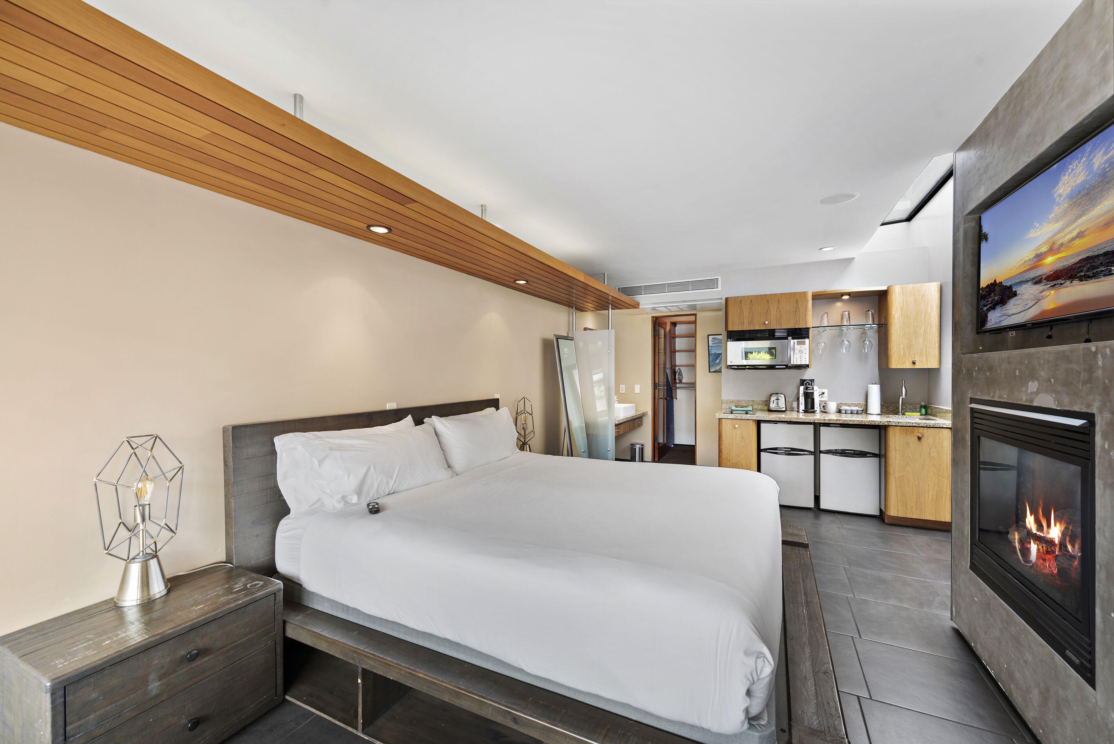 A modern hotel room with a large bed, a small kitchenette, and a fireplace.