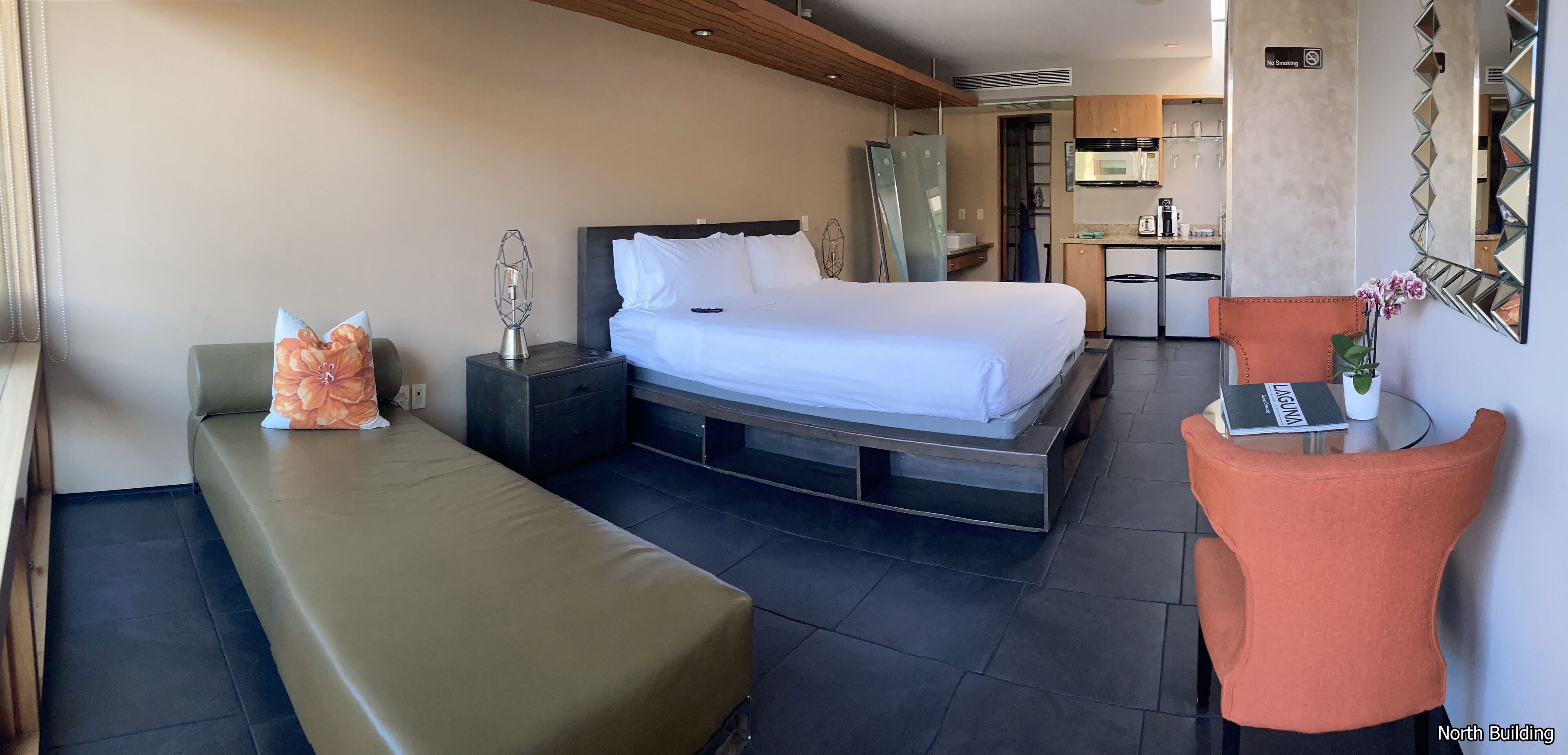 A modern hotel room with a bed, bedside table, lamp, and a small seating area.