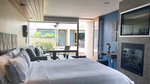 Une chambre d’hôtel moderne dotée d’un grand lit, d’un coin salon avec une table et des chaises, d’une cheminée et d’une vue sur l’espace extérieur.