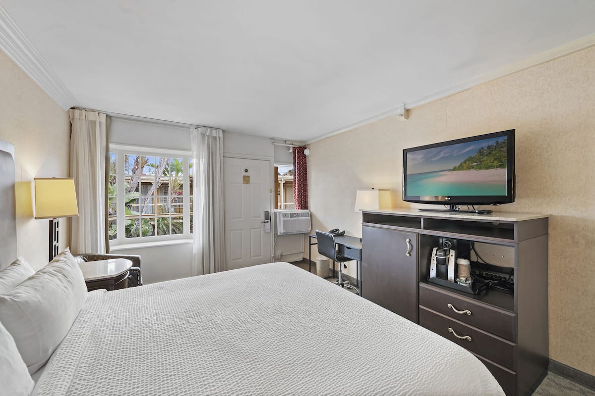 A hotel room with a large bed, a desk, a television, and a window with curtains.