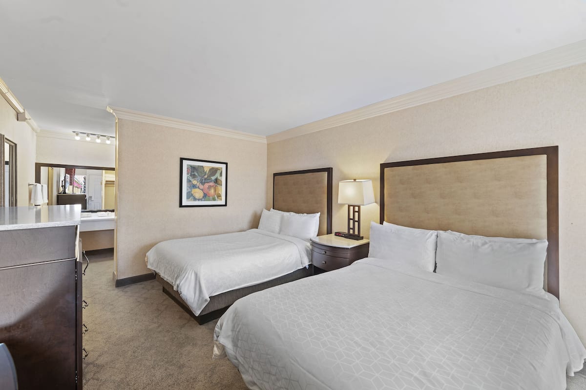 A hotel room with two single beds, a dresser, a nightstand with a lamp, and a framed picture on the wall.