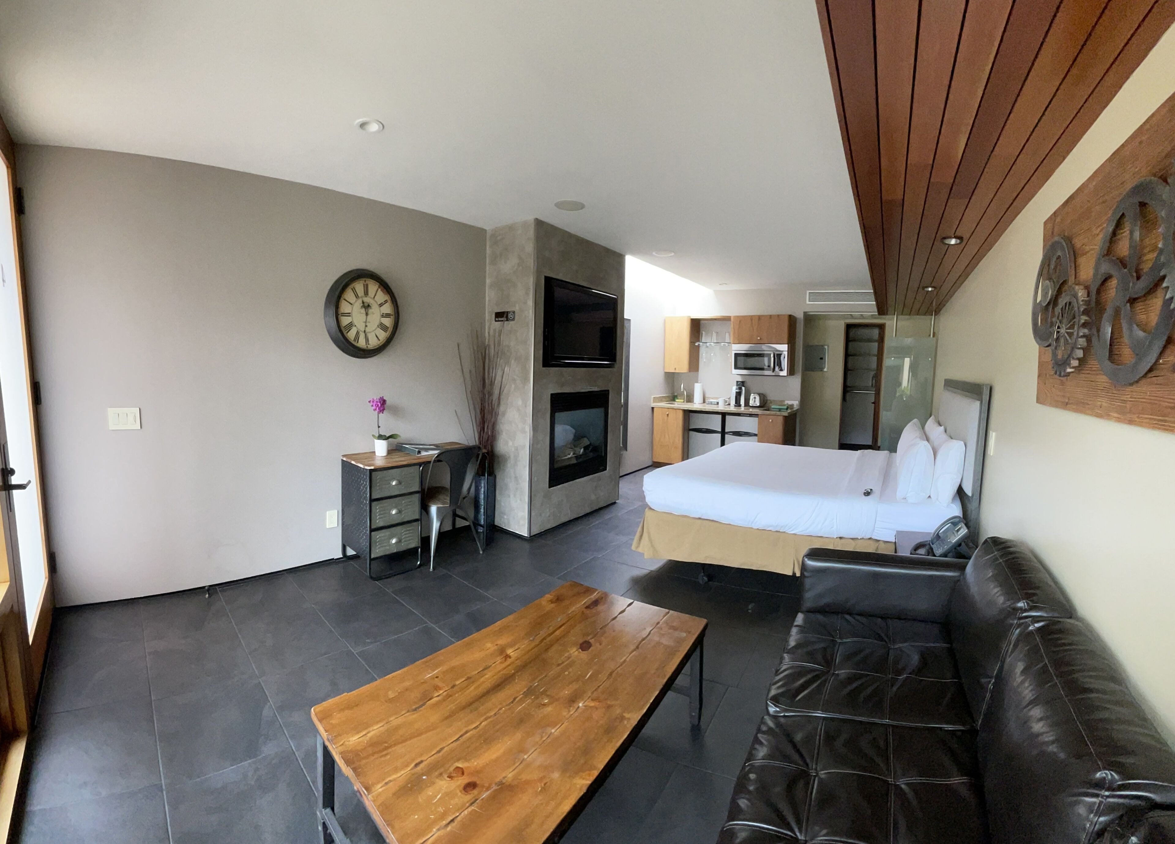 A compact living space with a kitchenette, a bed, a sofa, and a wooden table.