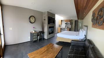 A compact living space with a kitchenette, a bed, a sofa, and a wooden table.