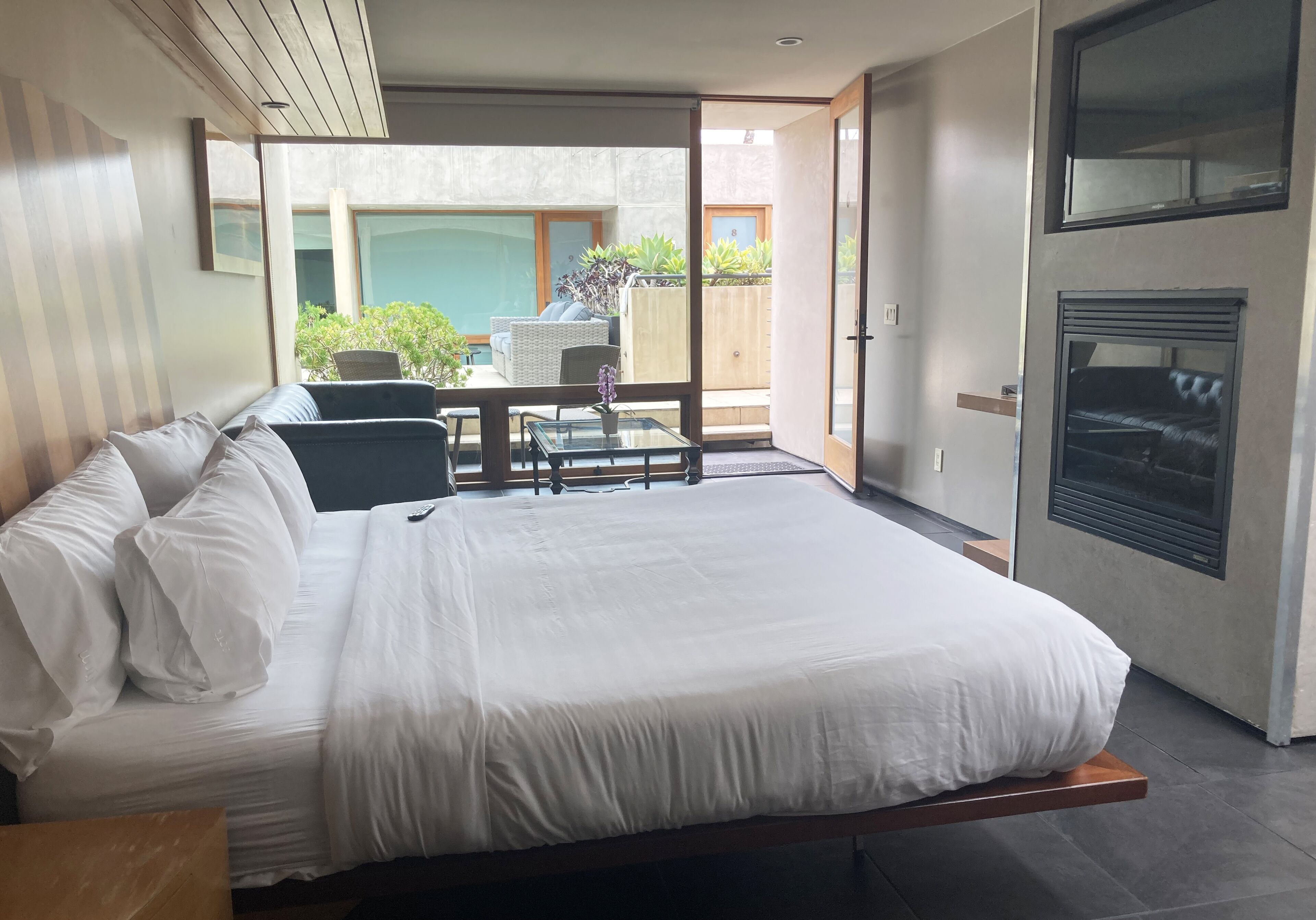 A modern bedroom with a large bed, a glass table, and a view of the outdoor patio.
