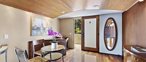 A modern interior with a wooden ceiling, a round dining table with chairs, a potted plant, and a large mirror.