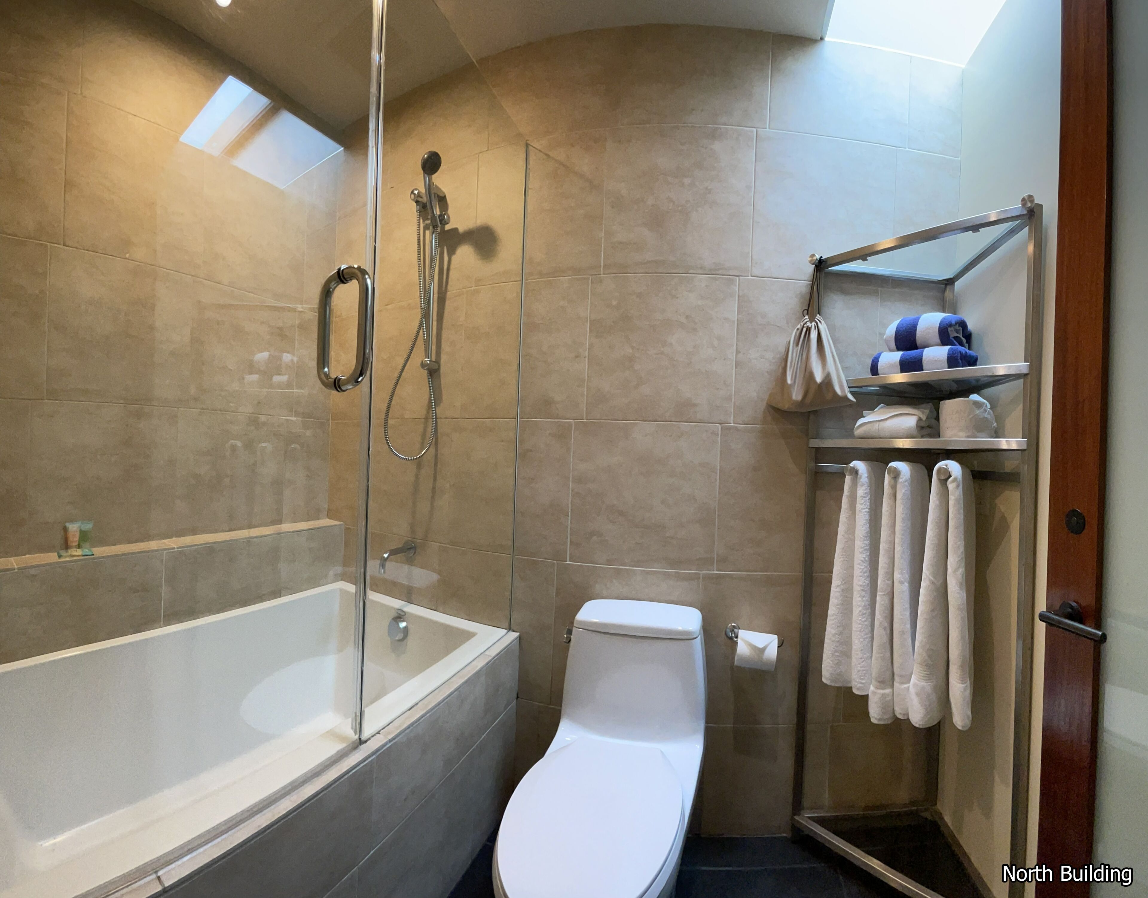 Un baño moderno con ducha envuelta en vidrio, inodoro blanco y toallero con toallas ordenadas.