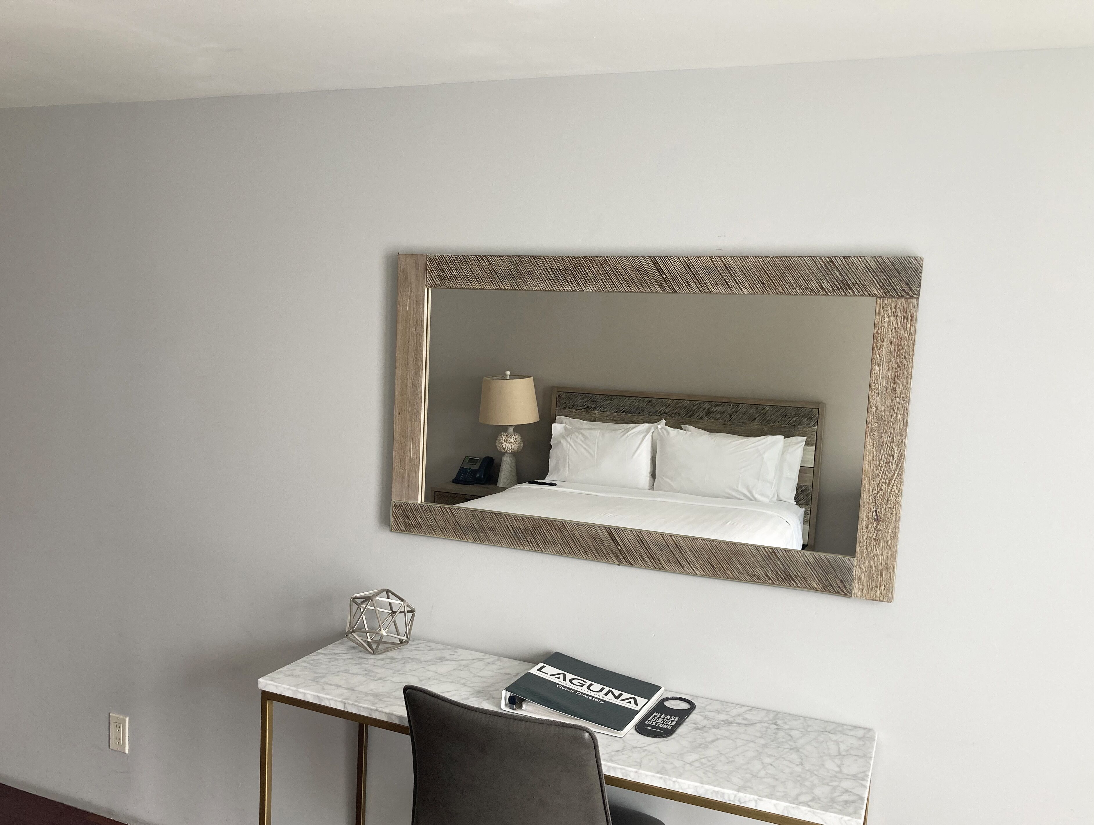 A hotel room with a bed, a bedside table with a lamp, a phone, and a desk with a chair.