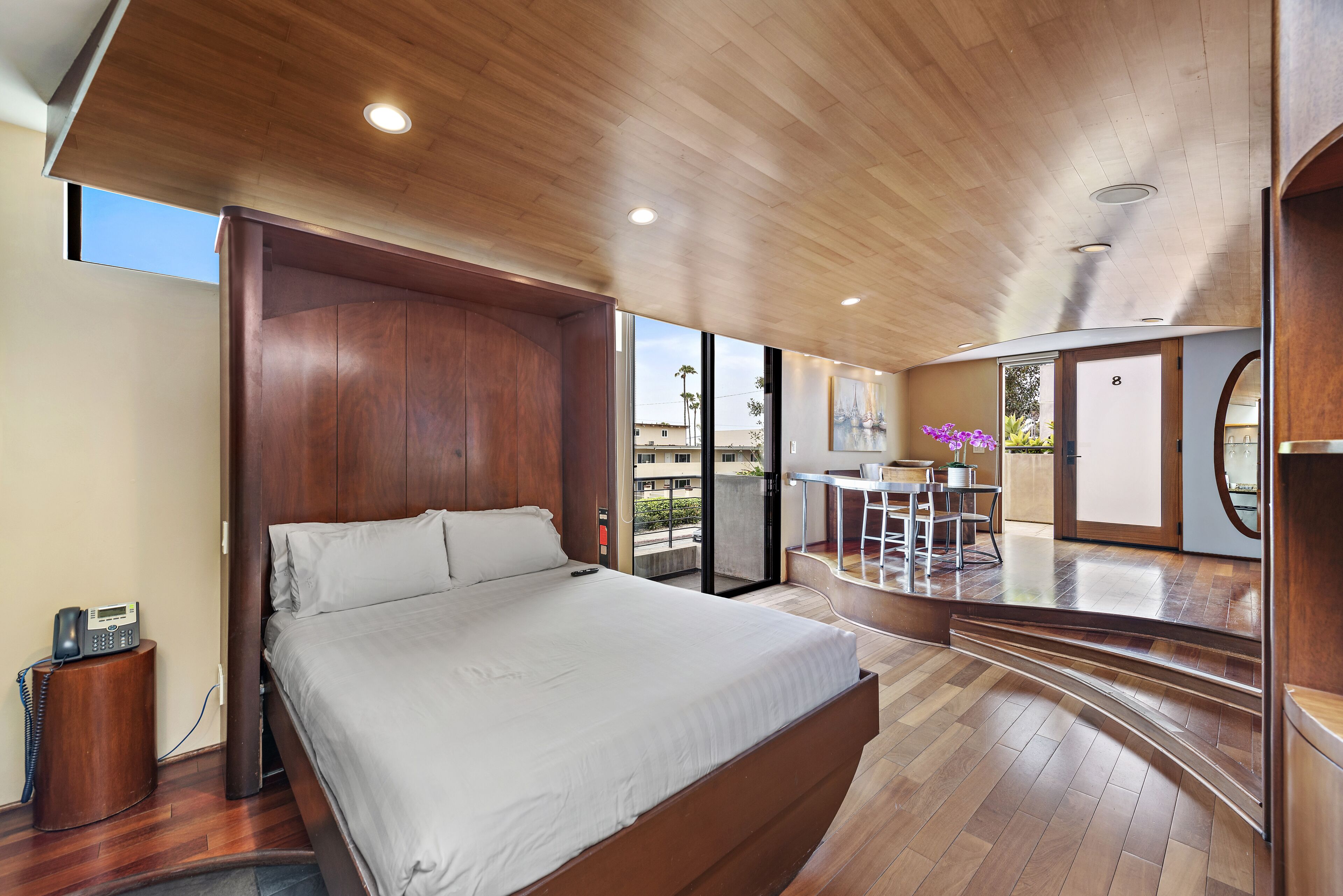 Ein modernes Schlafzimmer mit einem großen Bett, Holzboden und einem Balkon mit Essbereich.