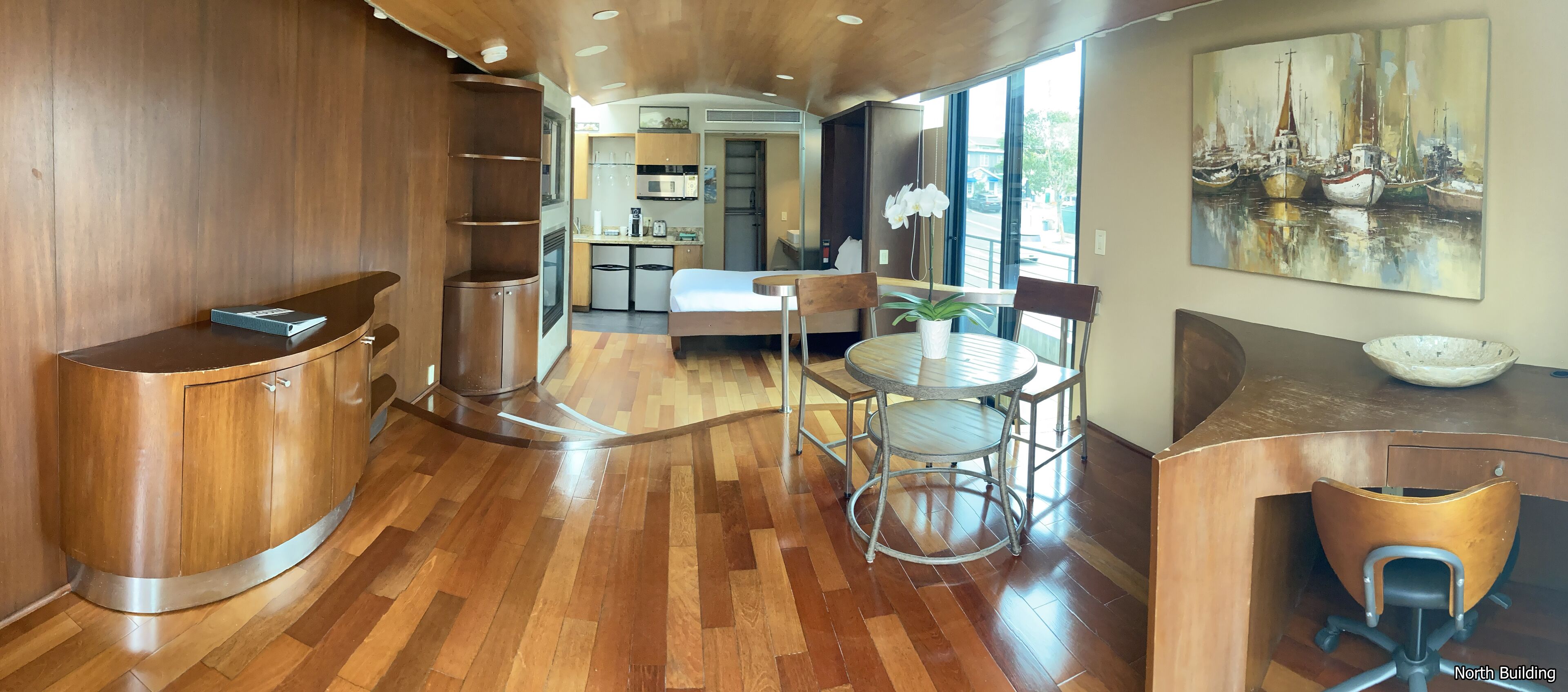 A modern kitchen with wooden cabinetry, a dining area with a round table and chairs, and a large window providing a view of the outside.