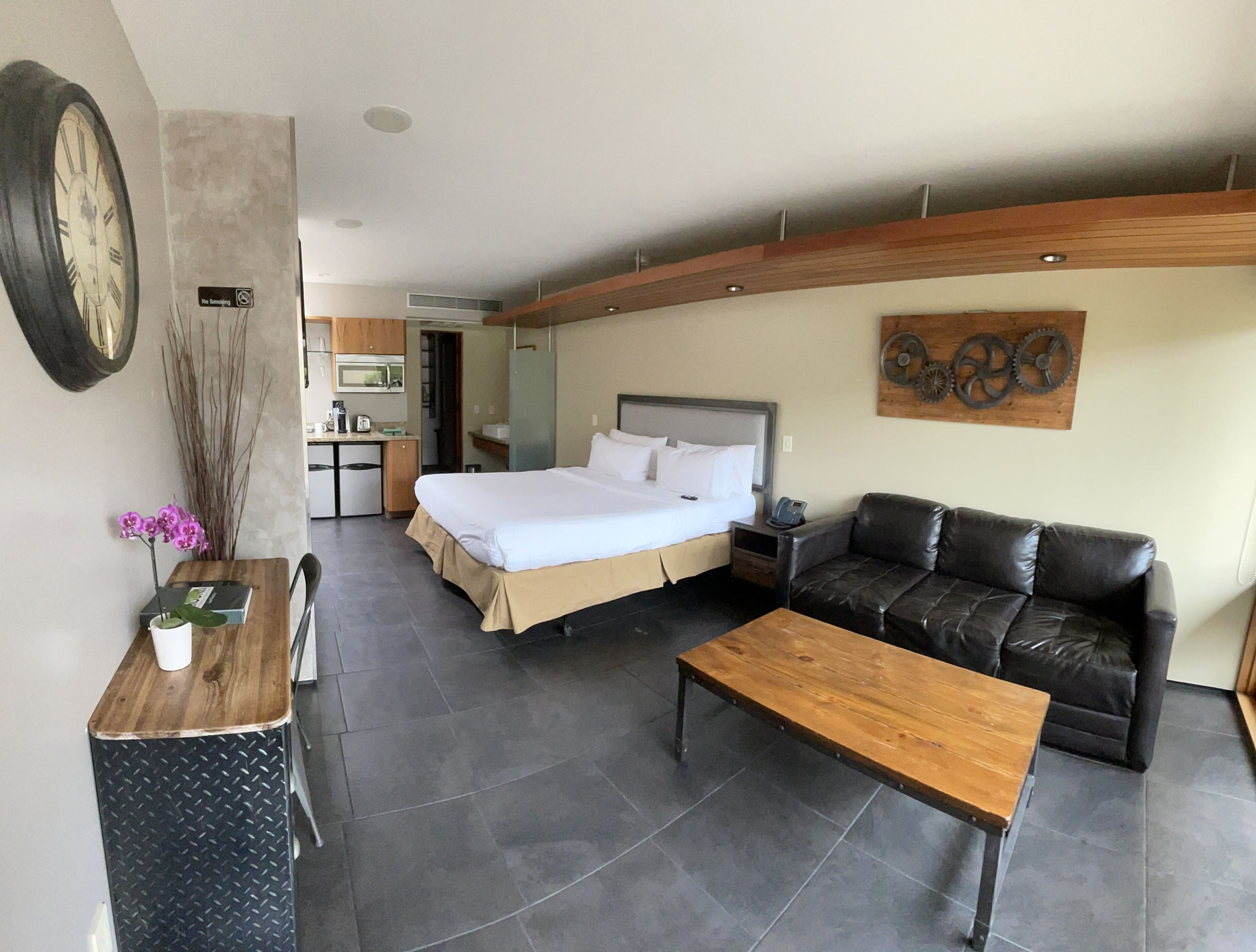 A hotel room with a bed, a leather sofa, a wooden table, a small desk with a chair, and a dining table with chairs.