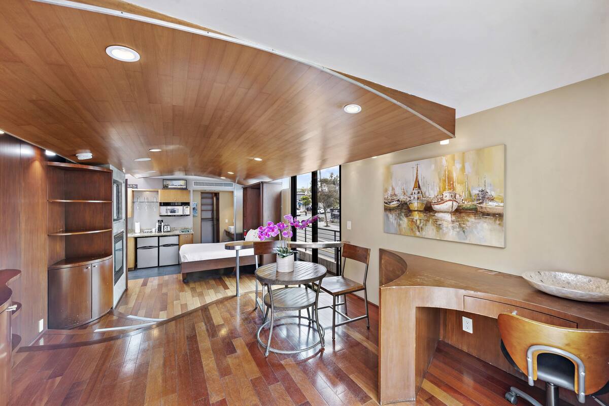 A modern kitchen with wooden flooring, a dining area with a round table and chairs, and a large painting on the wall.