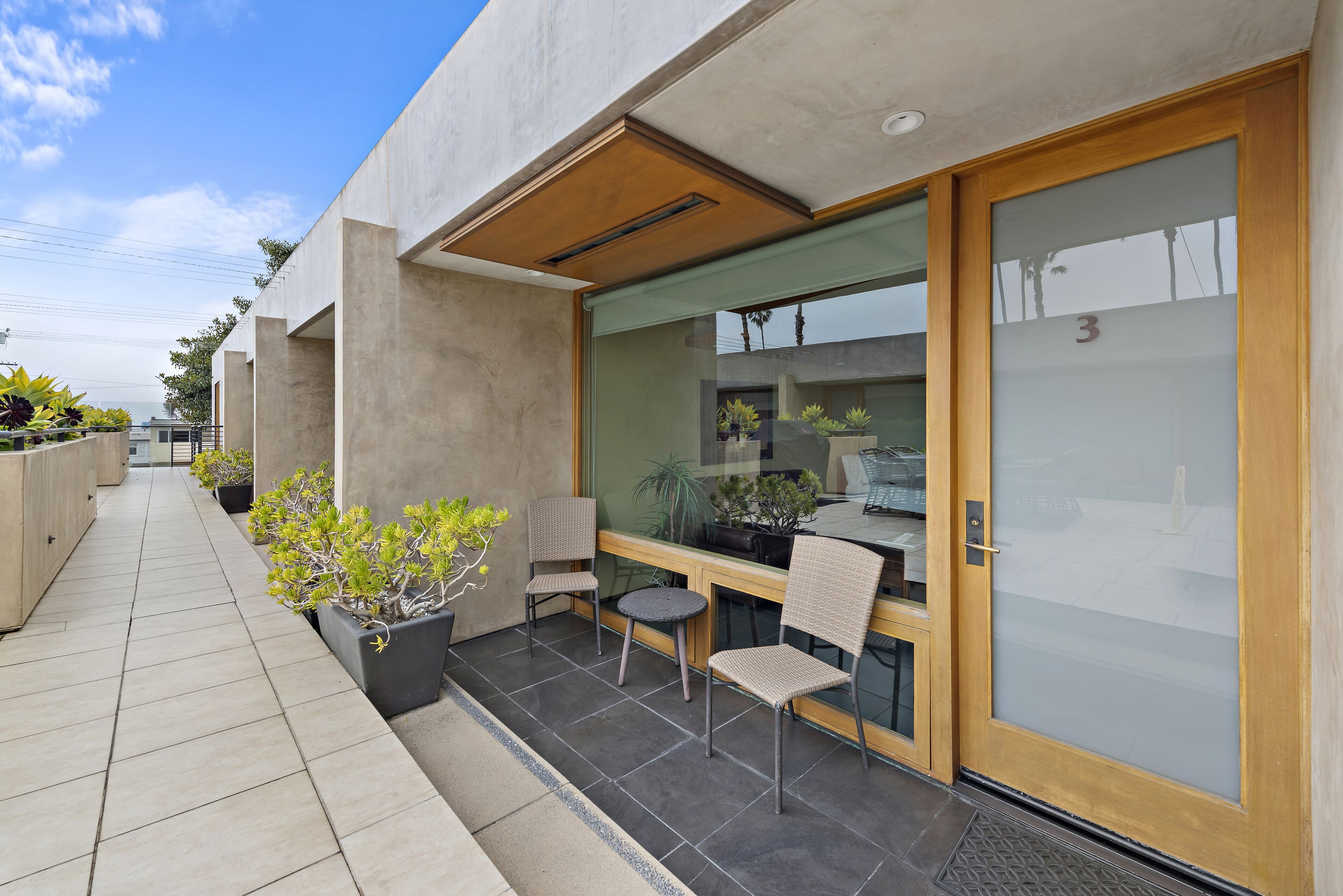 A modern building with a glass door, a small outdoor seating area with two chairs and a table, and potted plants.