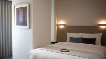 A hotel room with a neatly made bed, a framed picture on the wall, and a nightstand with a lamp.