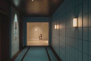 Un pasillo con suelo de baldosas, una puerta al final y luces en la pared.