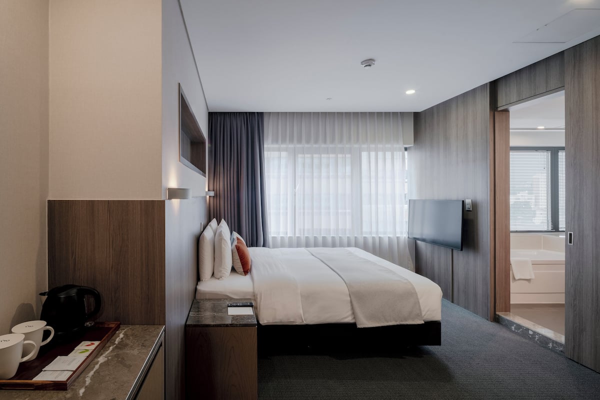 A modern hotel room with a large bed, a flat-screen TV, a coffee maker, and a view of the bathroom.