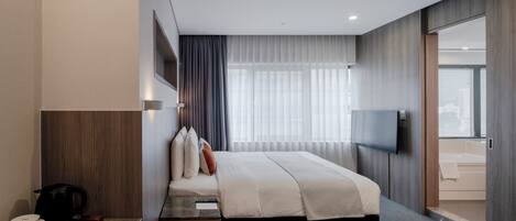 A modern hotel room with a large bed, a flat-screen TV, a coffee maker, and a view of the bathroom.