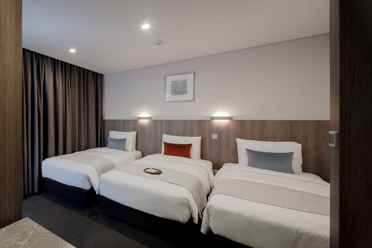 A hotel room with three single beds, a large window with curtains, and a framed picture on the wall.