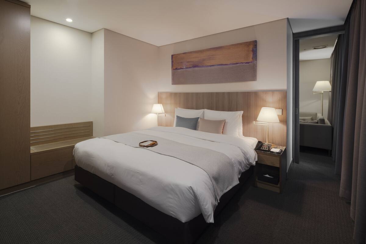 A hotel room with a large bed, bedside lamps, a wooden headboard, a painting on the wall, and a nightstand with a phone.