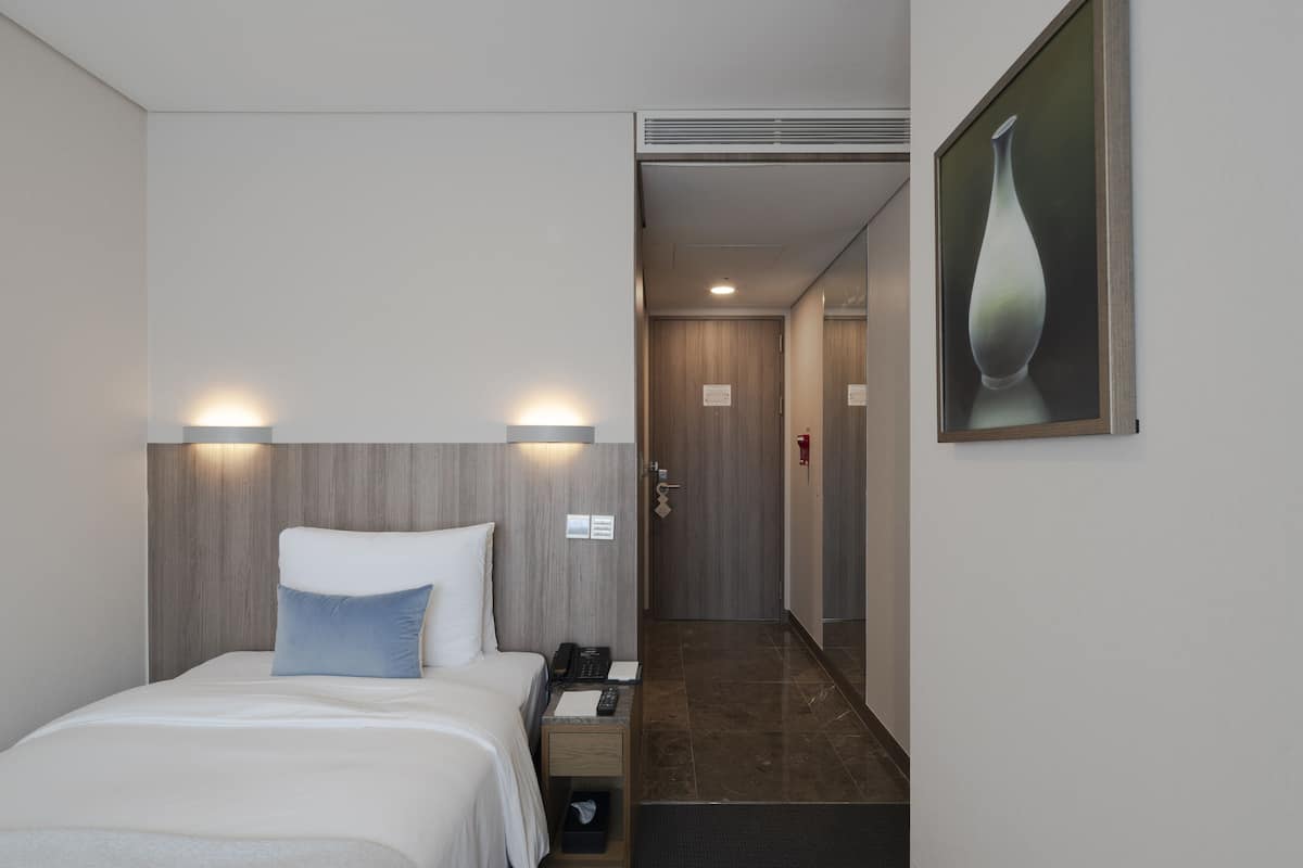 A hotel room with a bed, bedside lamp, nightstand, and a painting on the wall.