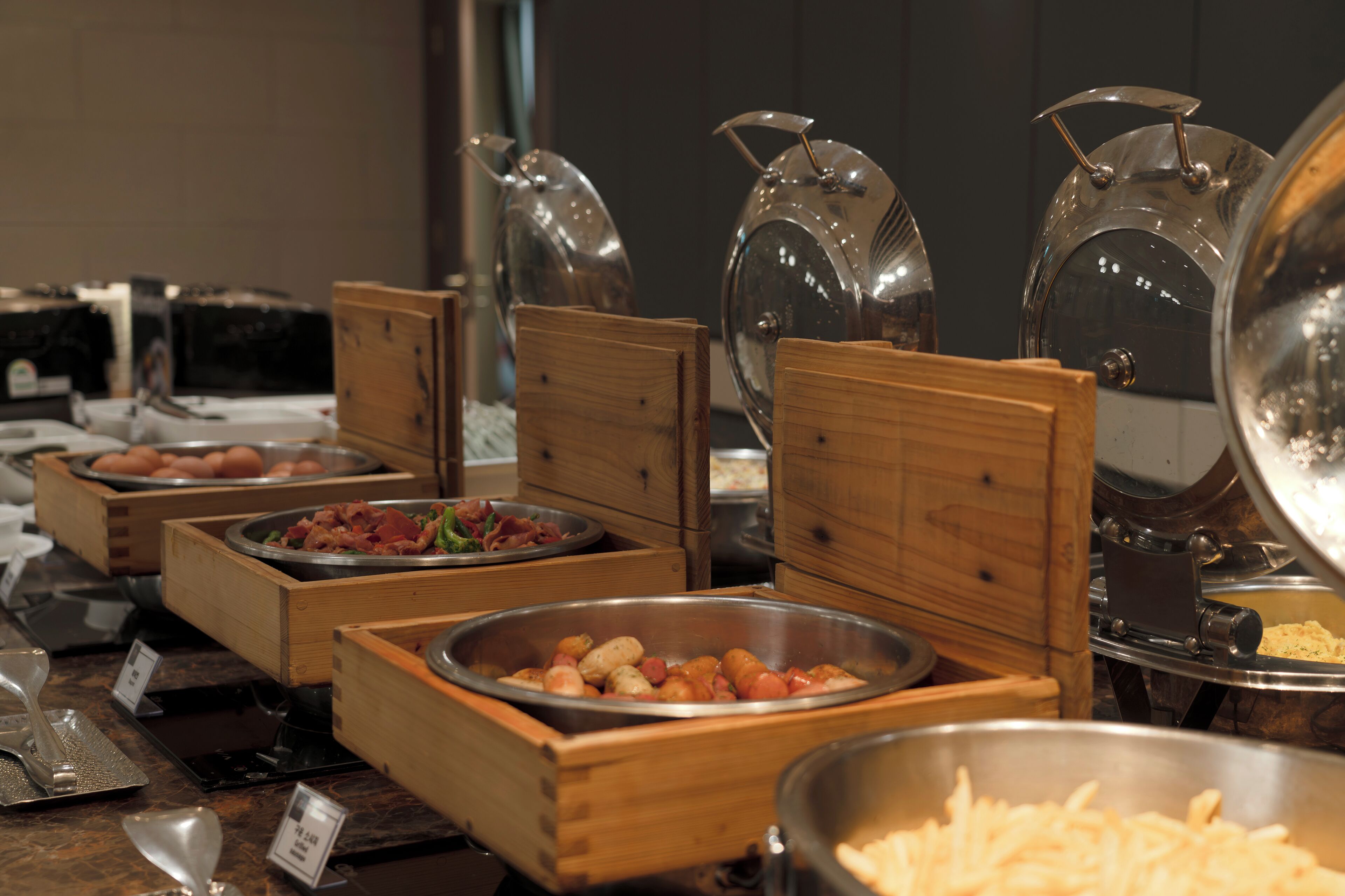 A buffet with various food items in wooden and metal containers, including a large bowl of pasta and a tray of eggs.