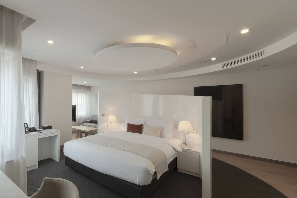A modern hotel room with a large bed, bedside tables, a desk, and a chair.