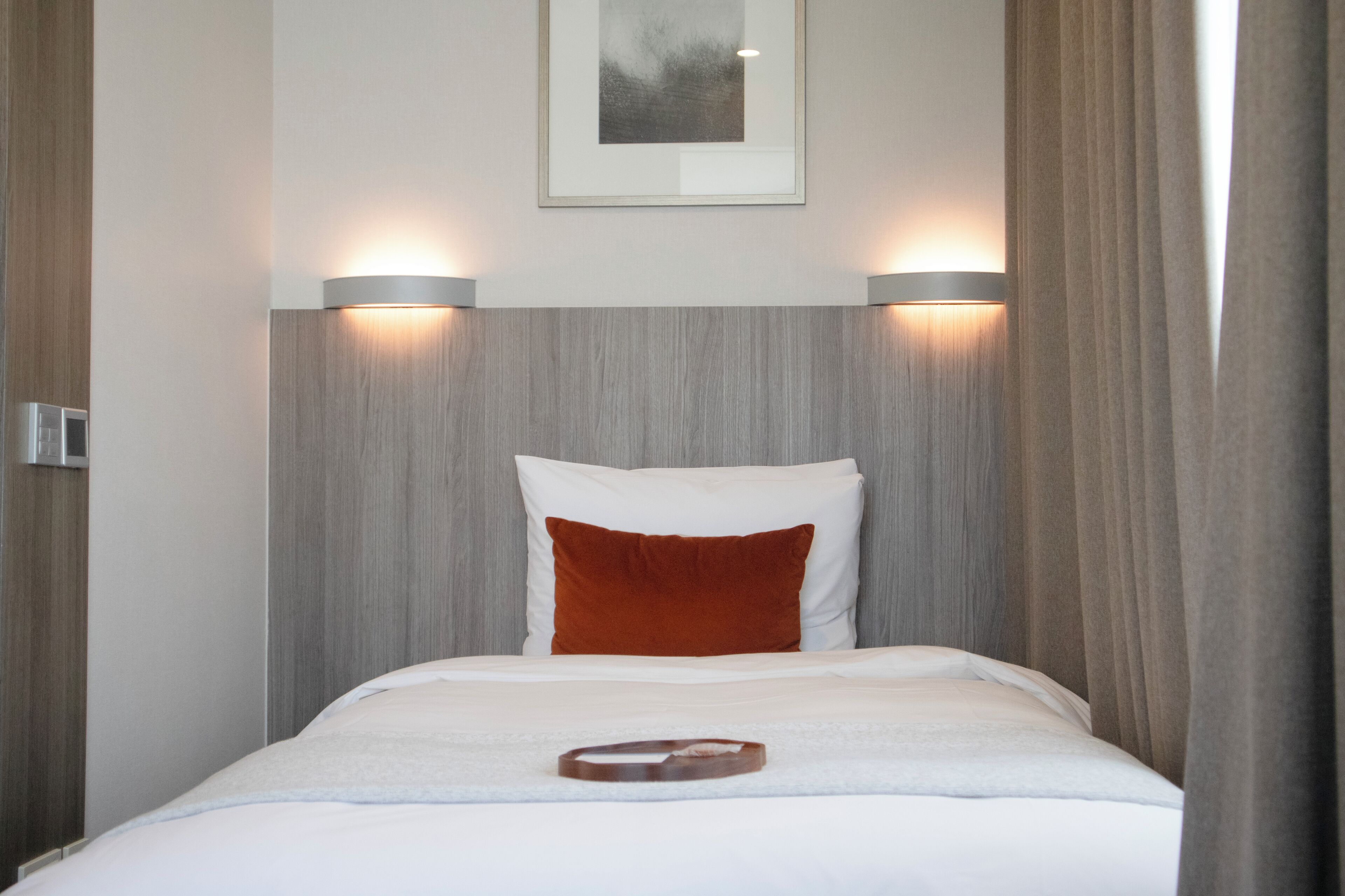 A hotel room with a bed, two wall-mounted lights, a framed picture on the wall, and a wooden headboard.