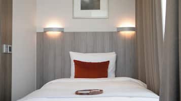 A hotel room with a bed, two wall-mounted lights, a framed picture on the wall, and a wooden headboard.