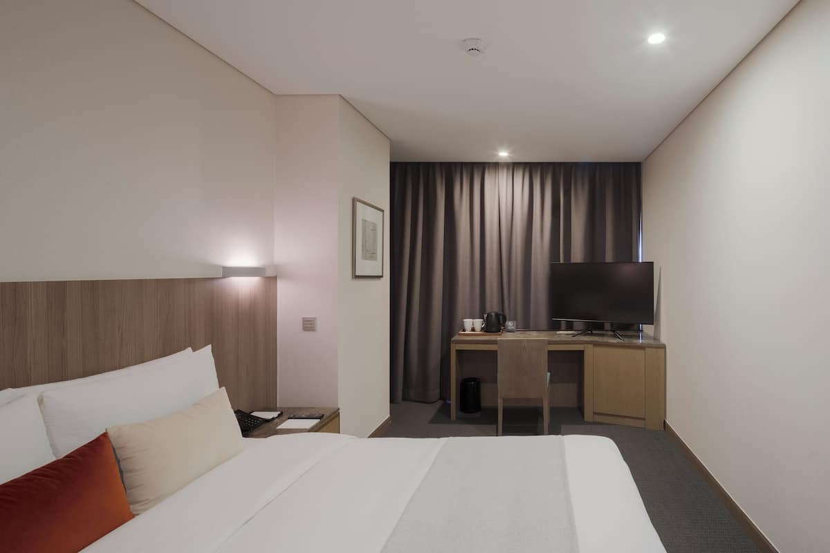A hotel room with a large bed, a desk with a flat-screen TV, a coffee maker, and a framed picture on the wall.