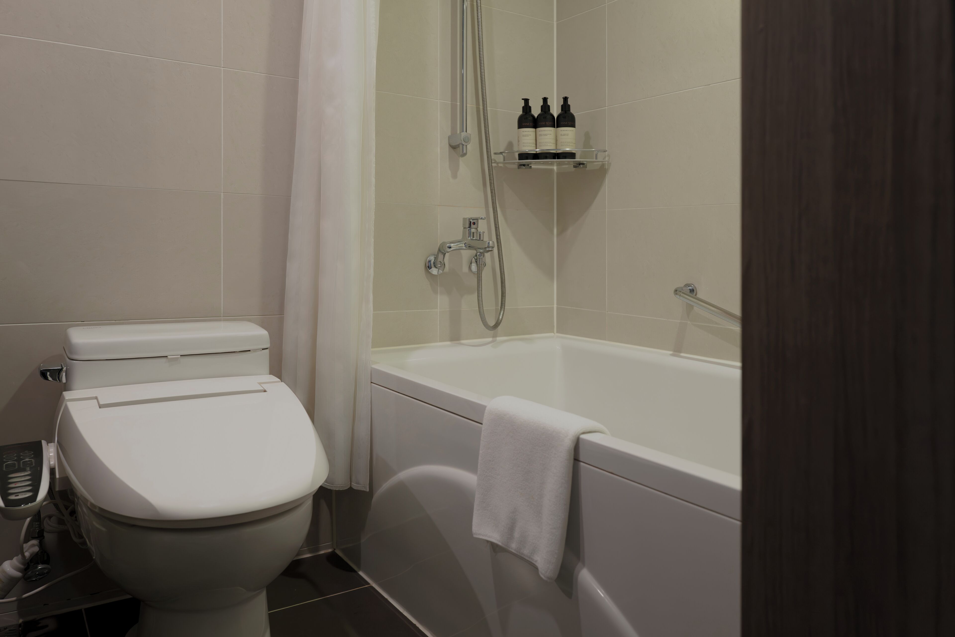 A modern bathroom with a toilet, bathtub, and shower. There are toiletries on a shelf above the bathtub.