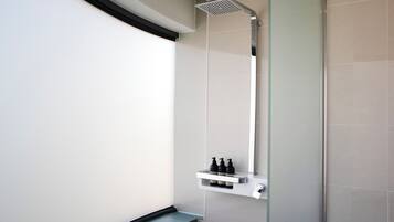 Un baño moderno con cabina de ducha de vidrio, estante blanco con artículos de aseo y un espejo grande.