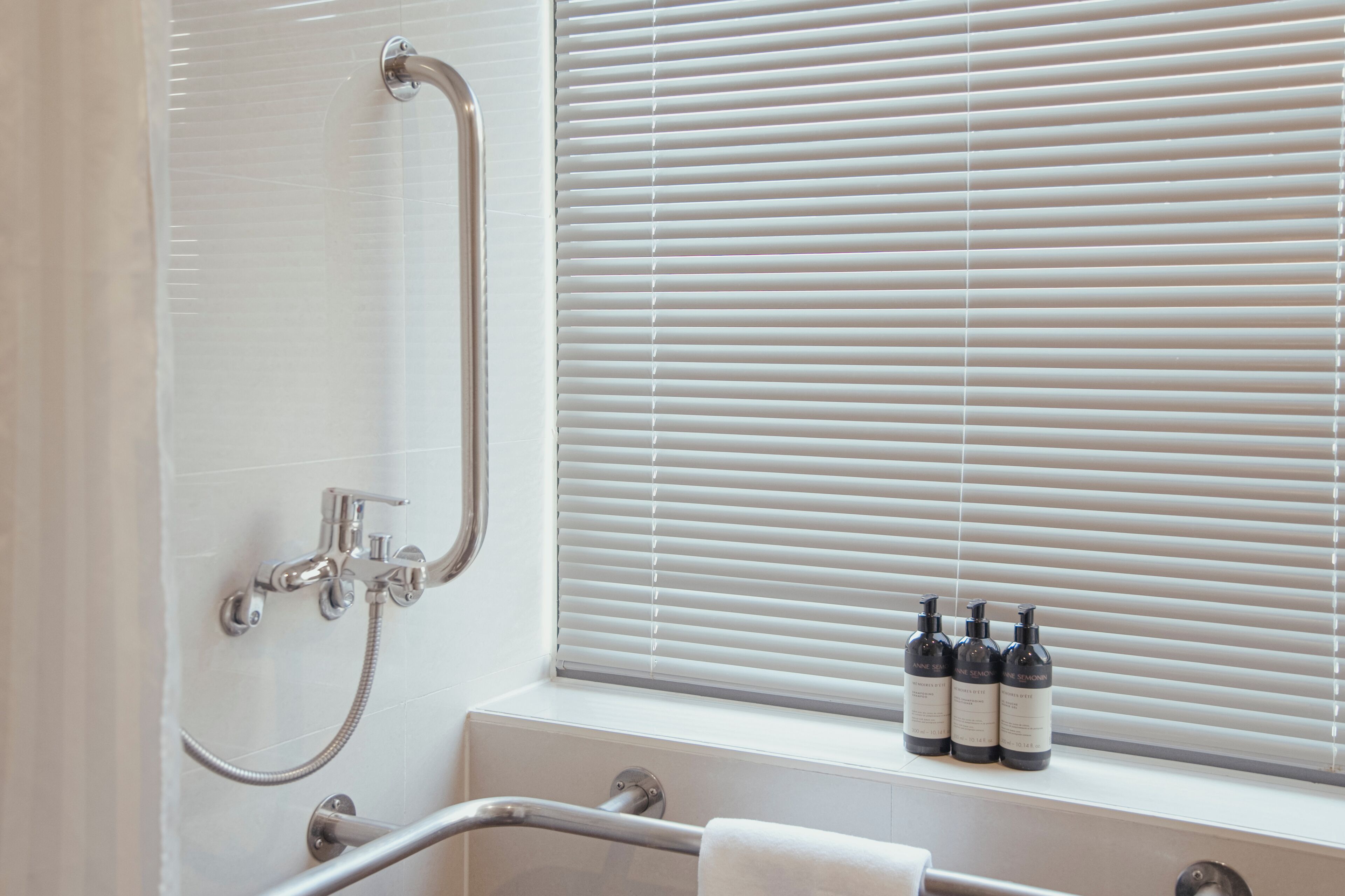 Un baño con ducha, una ventana con persianas y tres botellas en el alféizar.
