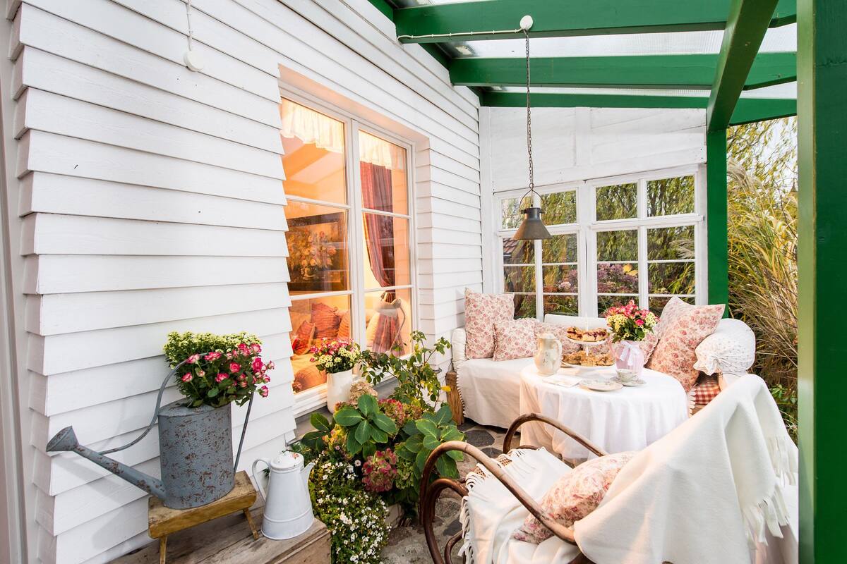 A cozy porch with white siding, a green roof, and a seating area with a table and chairs.