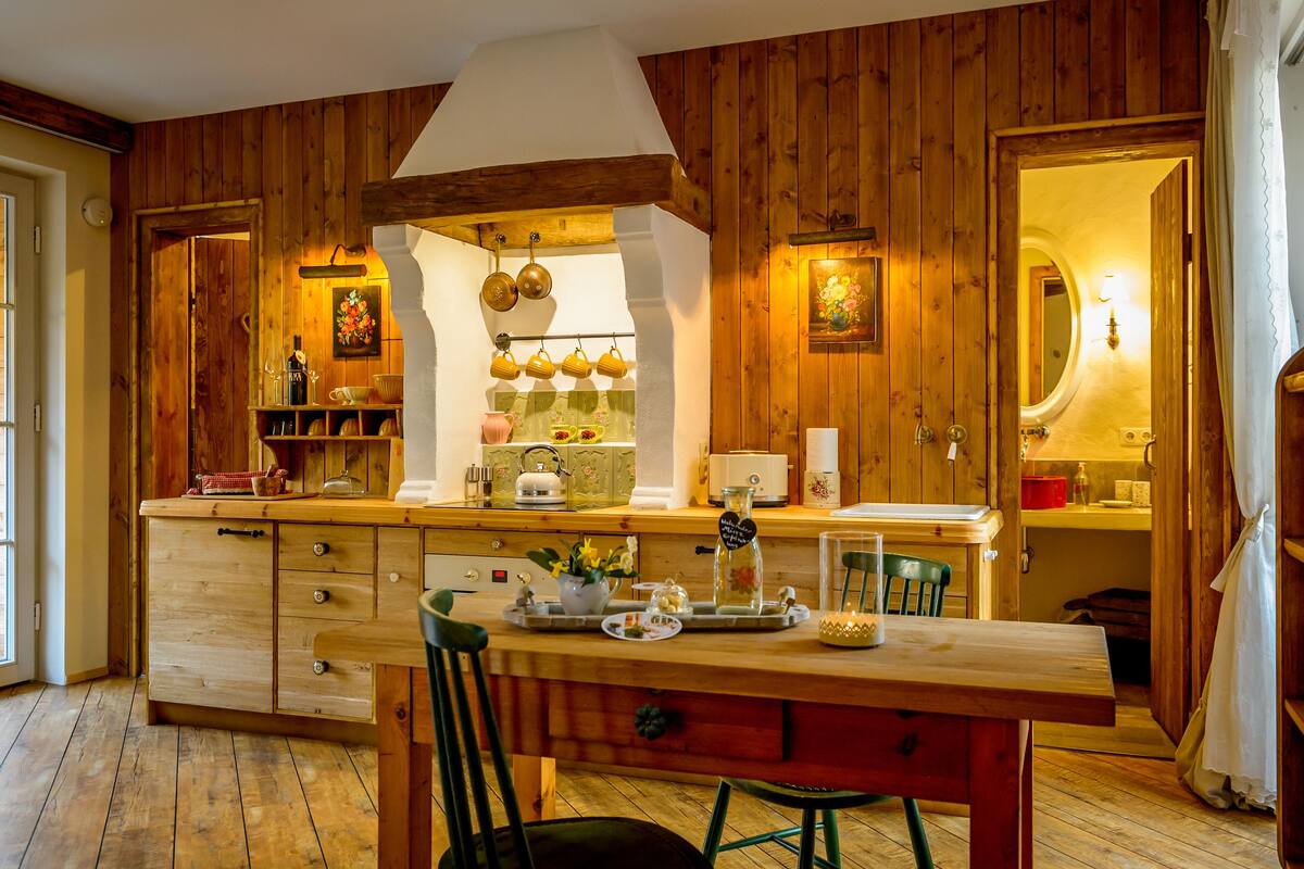 A wooden kitchen with a central island, a hanging pot rack, and a dining area with a table and chairs.