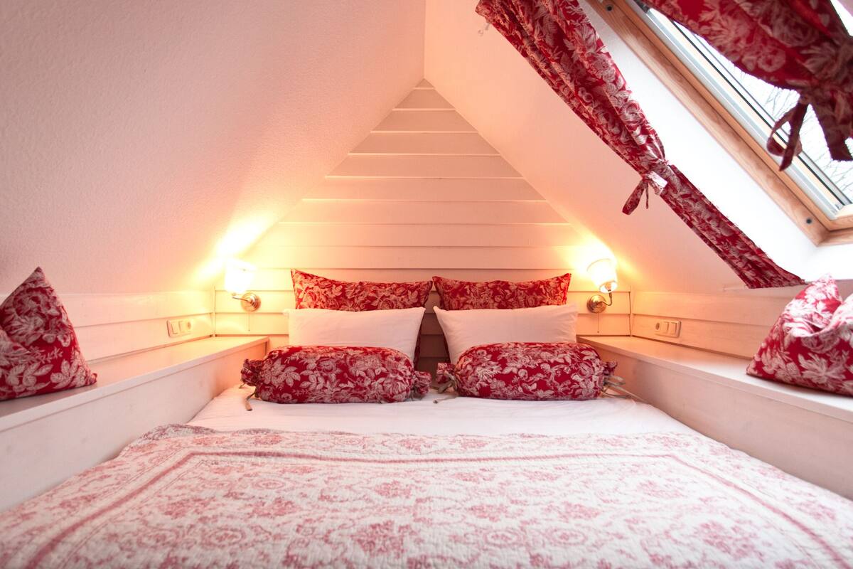 A bedroom with a sloped ceiling, floral-patterned bedding, and two bedside lamps.