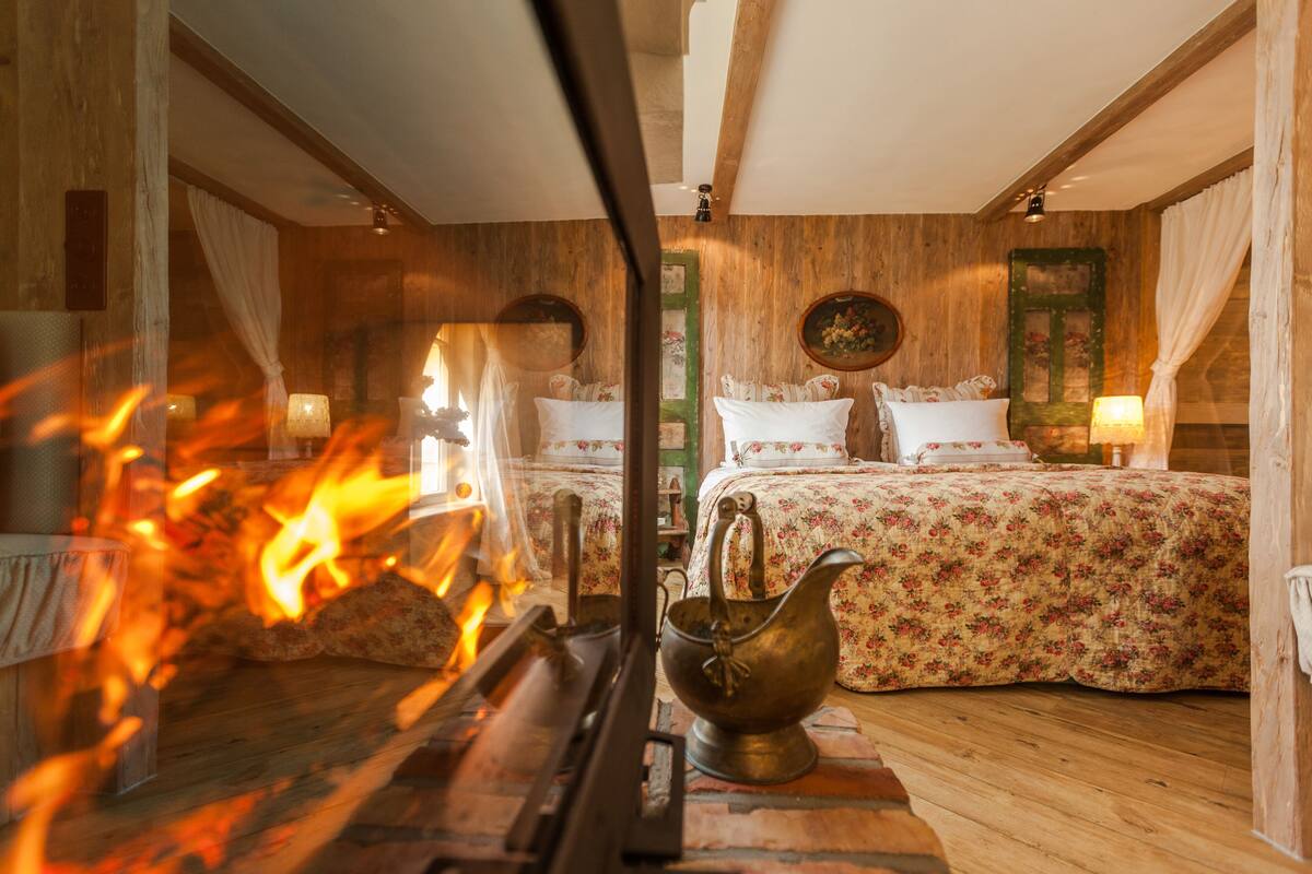 A cozy room with a fireplace, a bed with floral bedding, and a brass teapot on the floor.