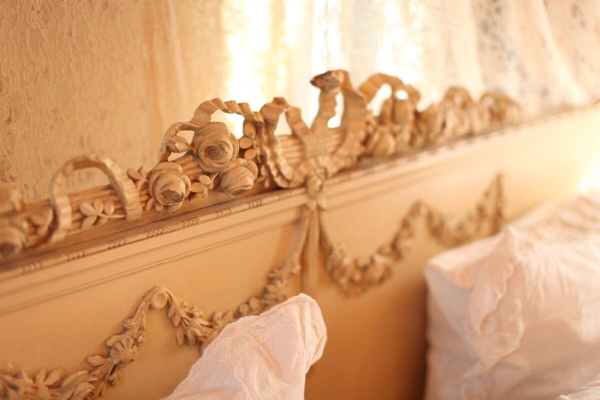 A room with ornate wooden carvings on the wall and a bed with white linens.