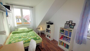 Una habitación pequeña y luminosa, con una cama, un escritorio y una estantería.