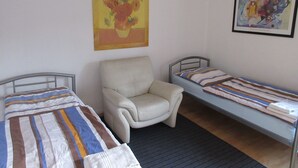 Una habitación con dos camas, una silla y dos cuadros en la pared.