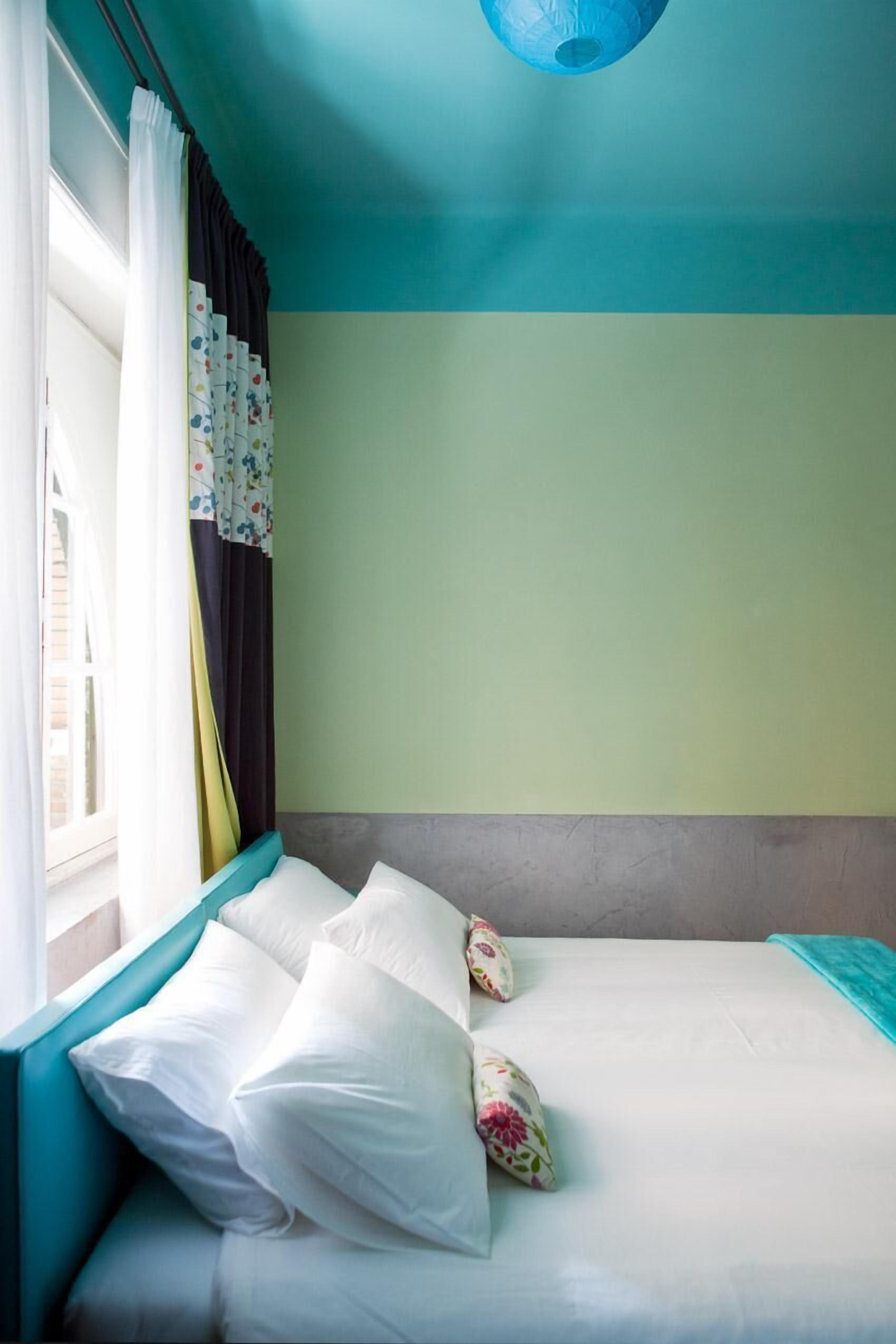 A room with a bed, a window with curtains, and a blue ceiling light.