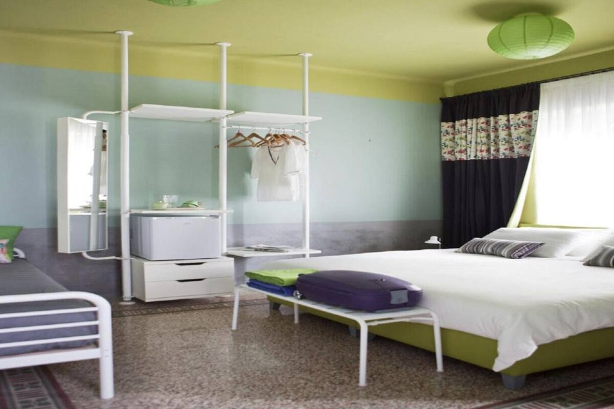 A bedroom with a bed, a wardrobe, a desk, and a hanging rack.