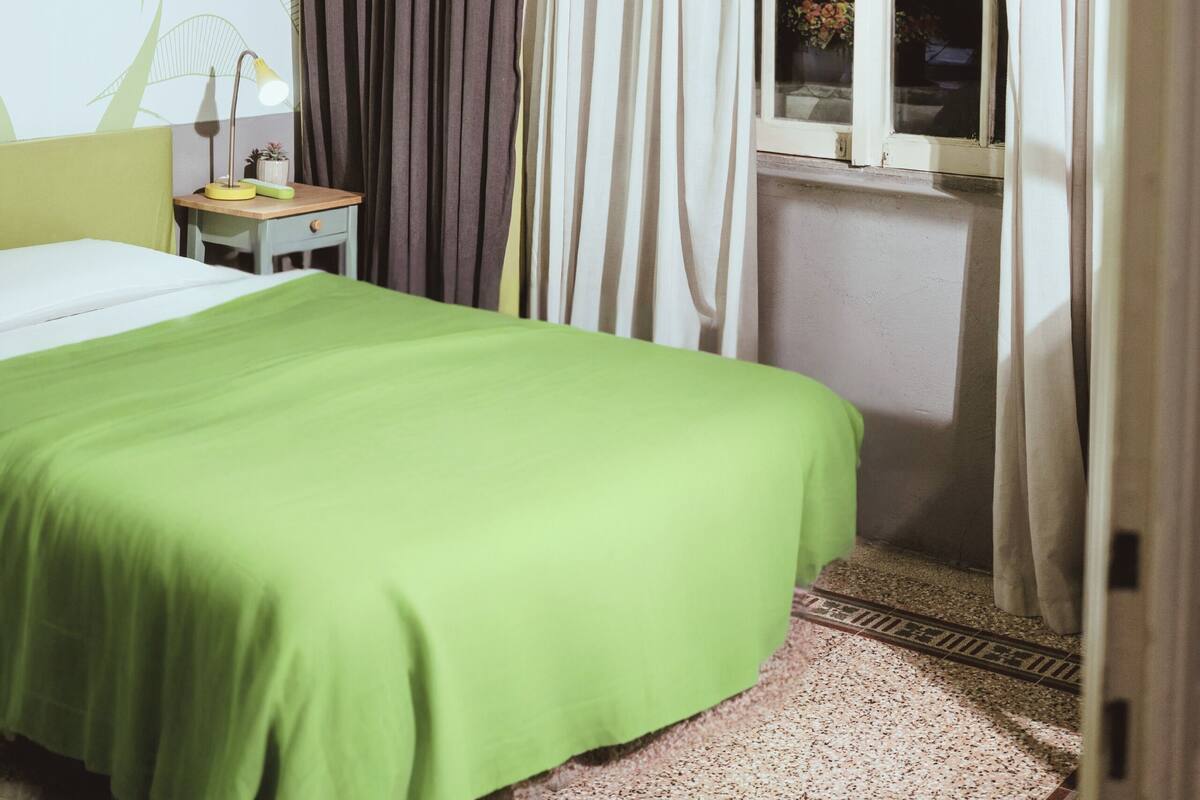 A room with a bed, a window with curtains, a lamp, and a wall with a leaf pattern.