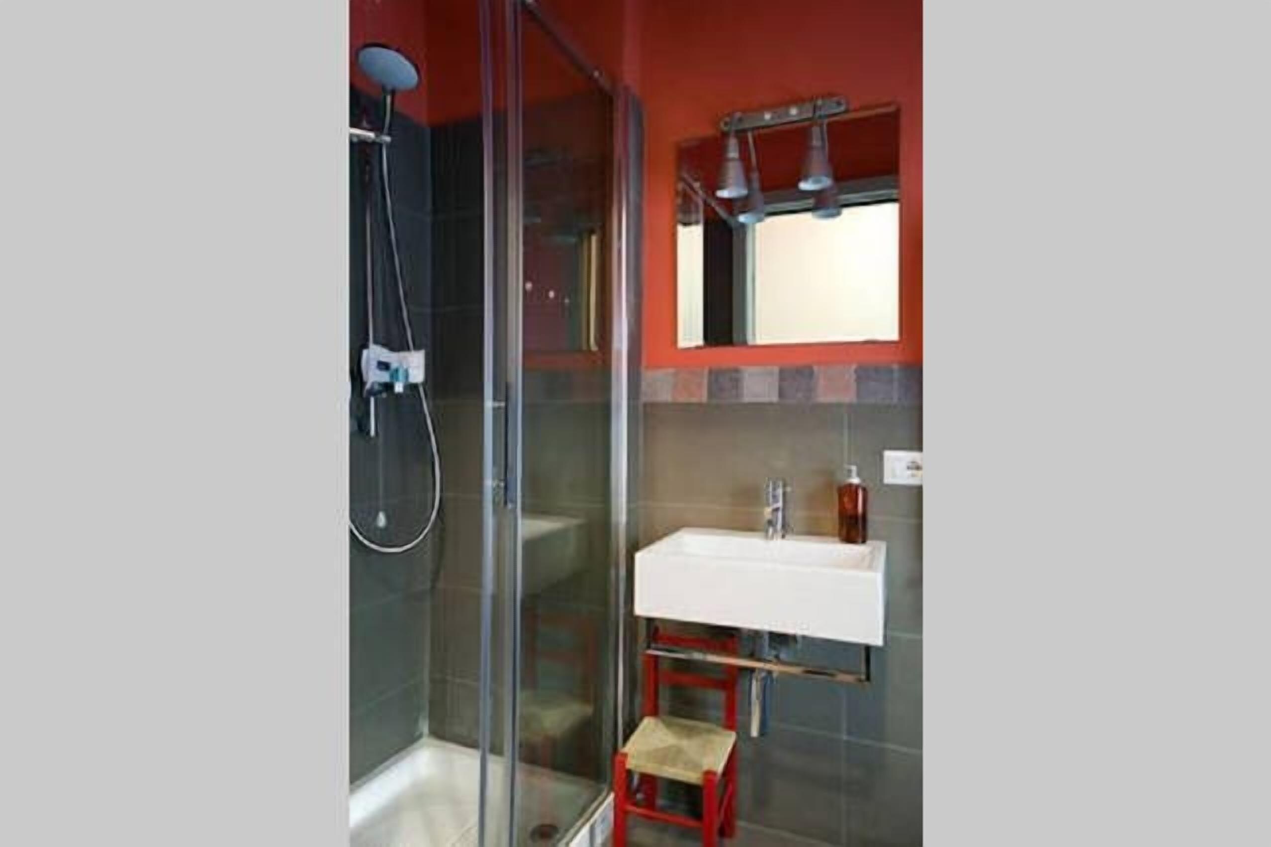 Une salle de bain moderne avec une douche à parois de verre, un lavabo blanc et un tabouret rouge.