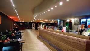 Un restaurante con mostrador de madera, mesas, sillas y plantas en macetas.