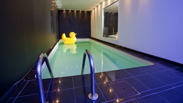 Una piscina con un pato inflable amarillo, escaleras metálicas para la piscina y un espejo grande en la pared.