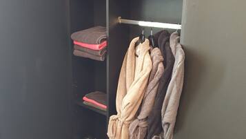 A closet with folded towels and robes, a shoe rack, and a metal hanger rack with robes.