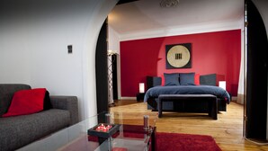 Un dormitorio moderno con una pared de acento roja, una cama grande, un sofá y una mesa de centro de vidrio.