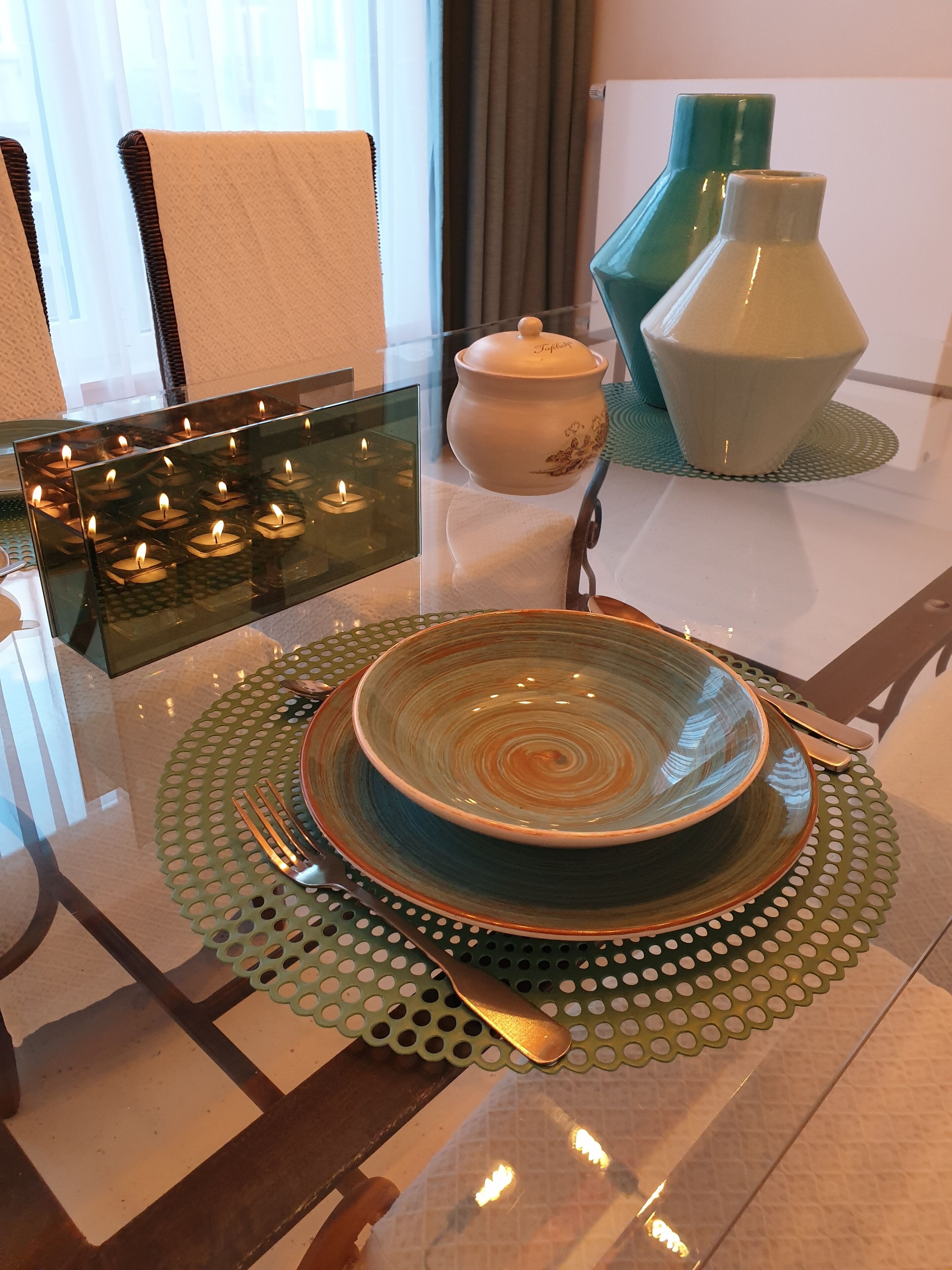 Una mesa de comedor dispuesta con un bol, platos, cubiertos y velas.