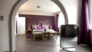 Un dormitorio con cama, mesitas de noche, televisión y ventana con cortinas.